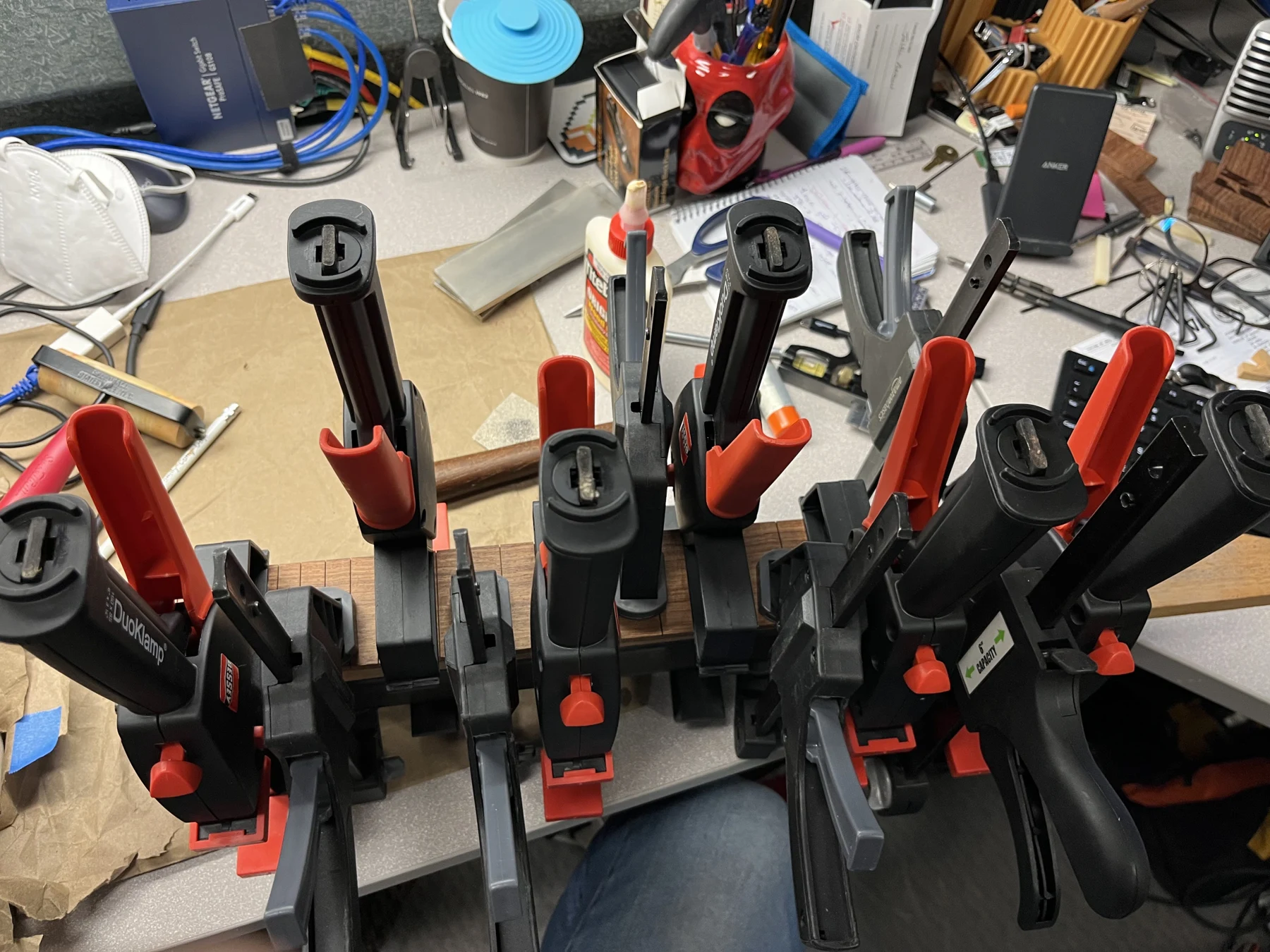 A fingerboard and neck held by an array of red and black clamps in the Moon & Pearl workshop